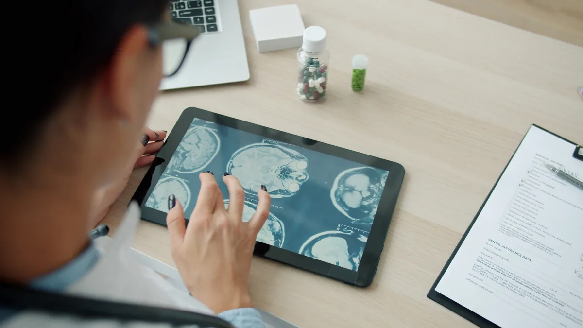 A clinician reviewing brain scan images on a tablet at a desk.